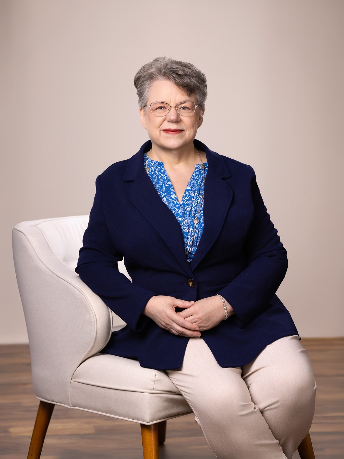 Wendy Cary - 202502 - 3x4 16 Wendy Cary sitting on the corner of a chair, leaning on the arm, with her hands resting in her lap.