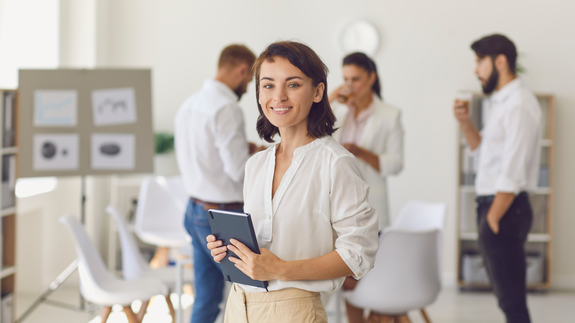 Confident woman starting new role with her team Professional woman holding a notebook, standing in front of colleagues in a conference room, symbolizing confidence in a new leadership role