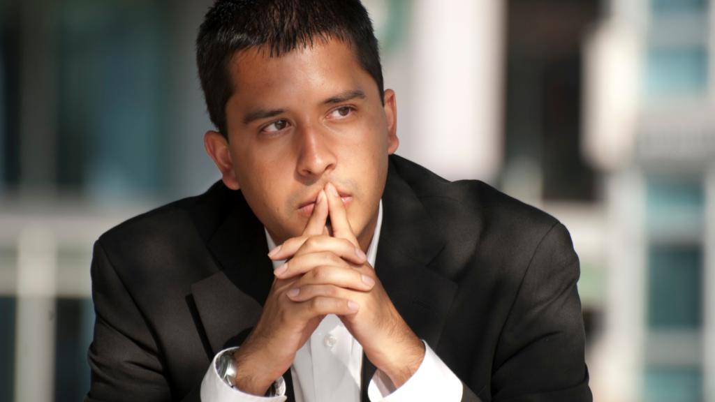Thoughtful leader in a suit with hands clasped near his mouth, looking off to the side.