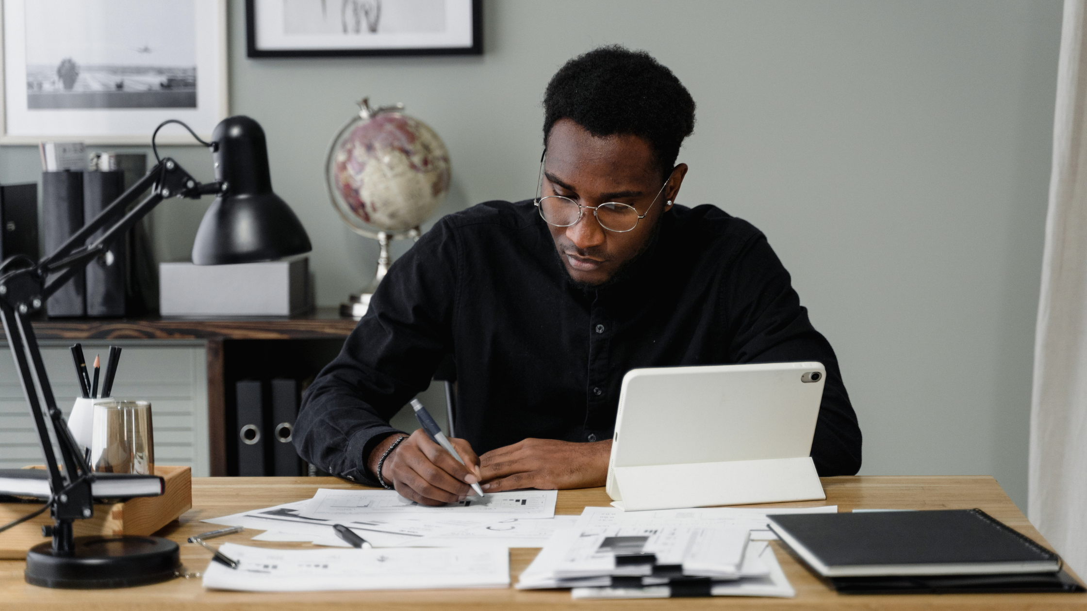 Professional writing notes at a desk with a tablet nearby.
